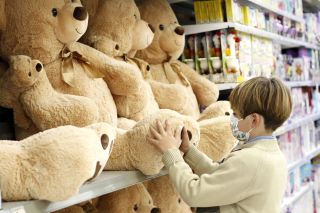 Little boy shopping in toy shop looking at teddy bears