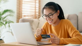 Young woman sitting at home using credit card to pay for something on a laptop