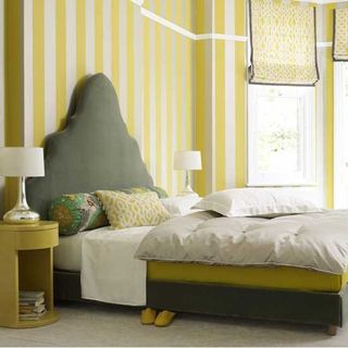 bedroom with yellow and white striped wall grey bed with designed cushions and white flooring