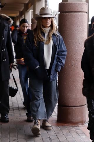 jennifer lopex wearing a coat, a turtleneck, a cowboy hat, barrel jeans, and boots