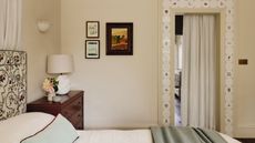 neutral bedroom painted in Farrow & Ball's Dimity with delft tile door trim, small vintage artwork, a floral upholstered headboard and a burgundy nightstand