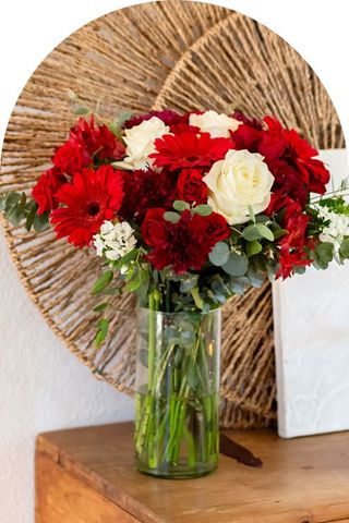 A bouquet of white and red flowers with greenery in a clear vase.