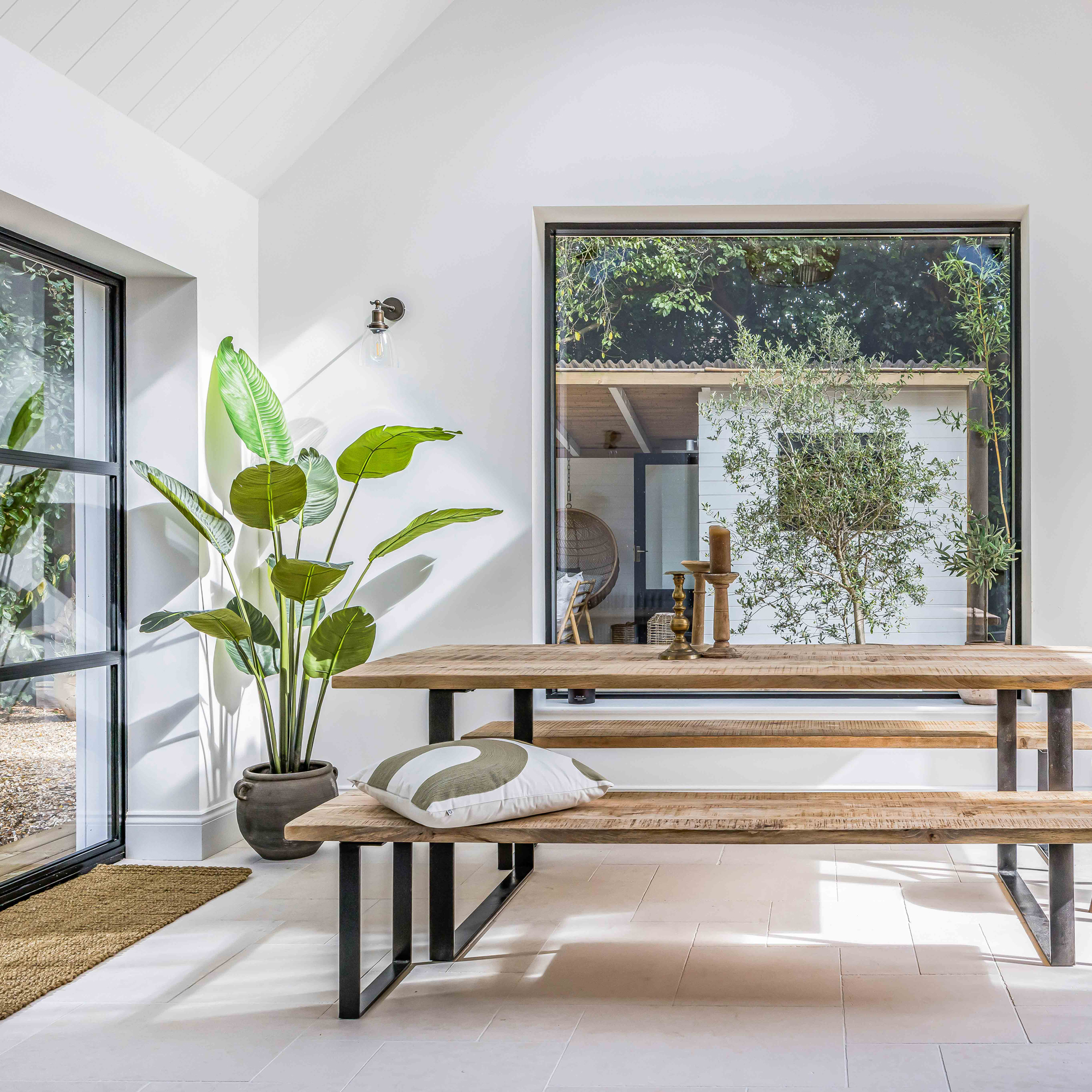 a dining room with a large picture window and patio doors, with a long wooden dining table and matching benches