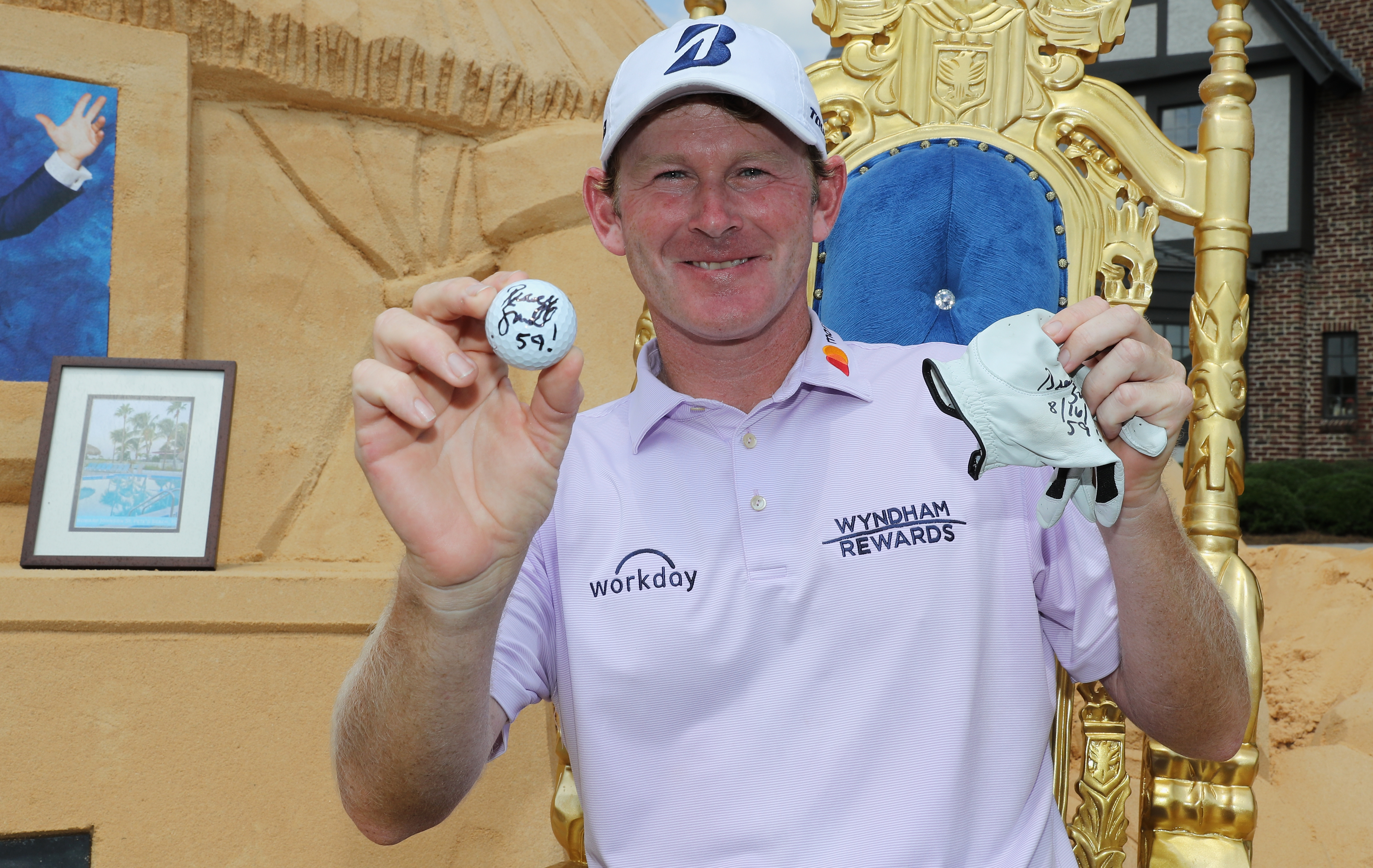 Brandt Snedeker holds up a golf ball and glove with 59 on it