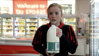 Máiréad Tyers in a red and black top as Jen in Extraordinary holds a carton of milk in a supermarket.