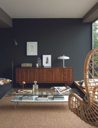 Black living room with mid-century wooden sideboard storage and glass coffee table.