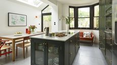 An open plan kitchen with a dining table, an island, and green cabinetry with brass hardware
