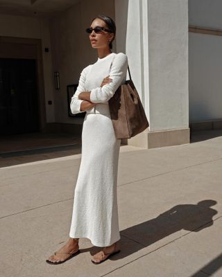 A woman wears a white long sleeve maxi dress with a waist belt and sandals.