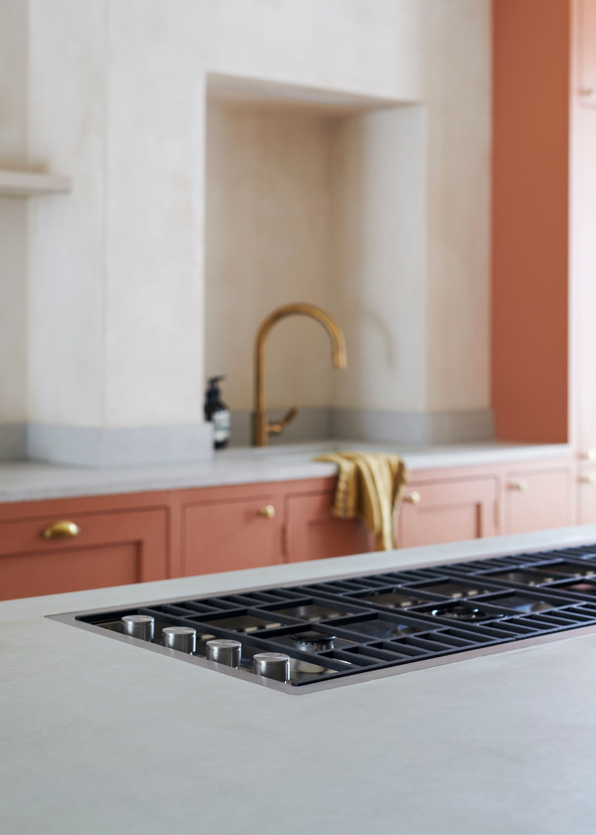 A close up shot of a kitchen with concrete worktops and a stove on top. There is also a slightly blurred view of a kitchen sink with brass hardware