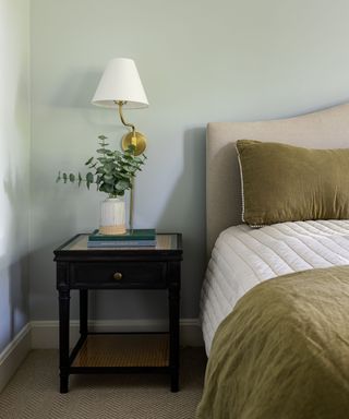 bedroom with light gray-green walls, neutral bed with white and khaki bedding and dark wooden nightstand