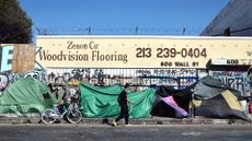 A person walks past an encampment of unhoused people in the Skid Row community on June 28, 2024 in Los Angeles, California