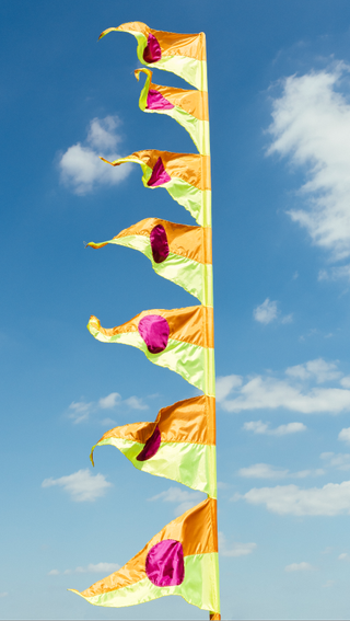 A colourful flag photographed against the blue sky, created by Yinka Ilori for Greenwich Peninsula