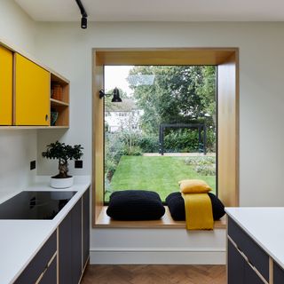kitchen with yellow cabinetry and a large picture window and window seat facing out into a garden