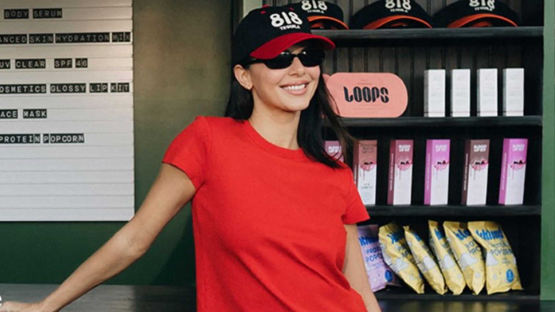 Kendall Jenner poses at a bar wearing dark wash jeans with white Derby shoes and a red t-shirt.