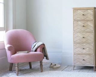 Pink Loaf Munchkin Chair in the corner of a bedroom with blanket draped over, beside tall chest of drawers