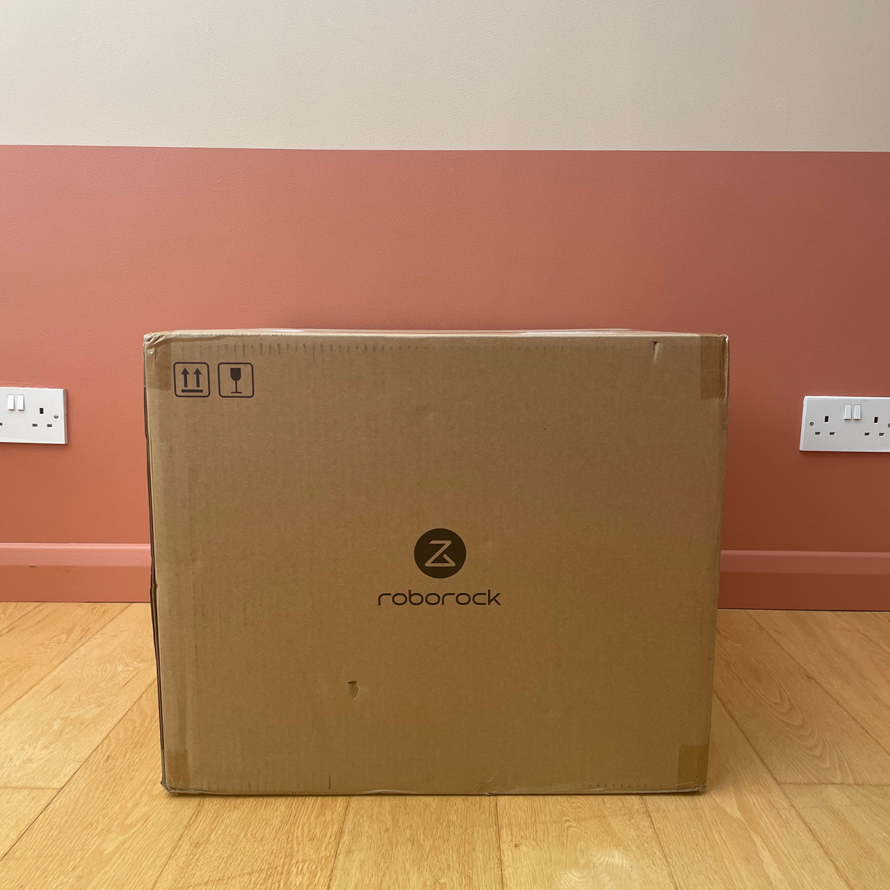 Roborock Qrevo Edge 2 Flow Robot Vacuum box sitting on wooden flooring in front of a two-tone pink wall