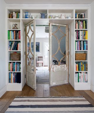 Bookshelving built around and above double doorway in room with white walls, wood floor, and striped rug