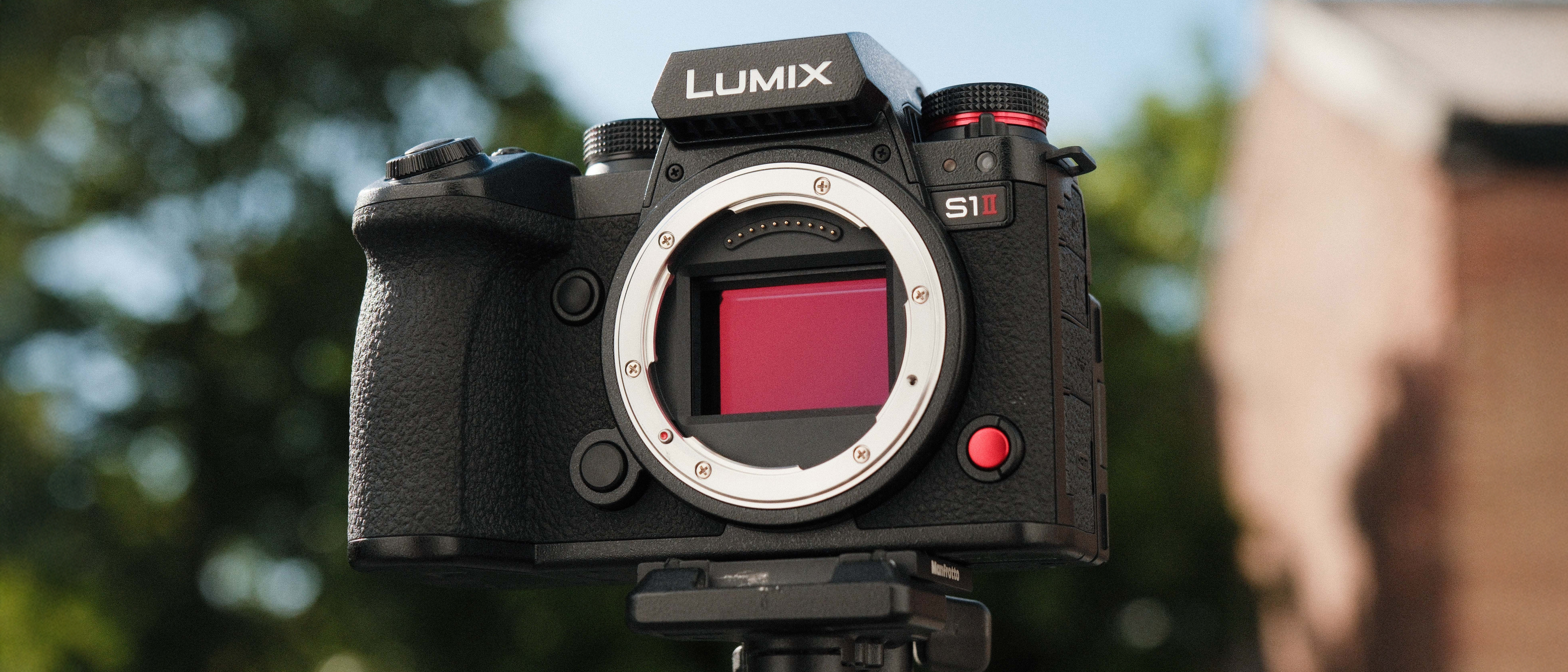 Panasonic Lumix S1 II camera on a tripod with green trees and blue sky in the background