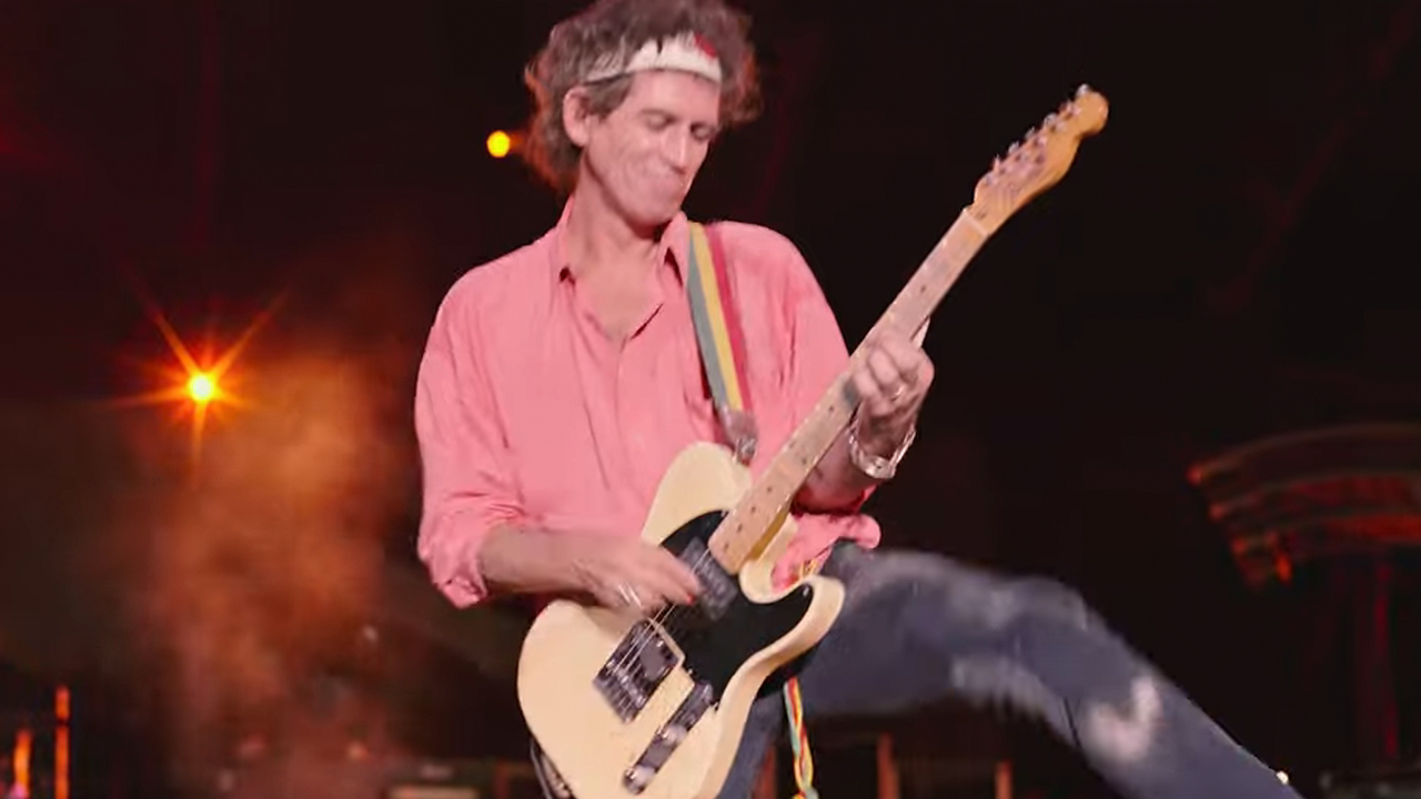 ピンクのシャツを着てステージでギターを弾くキース・リチャーズ