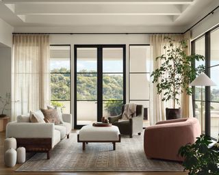 Modern living room with curved couches and neutral color scheme complementing forest view out large windows
