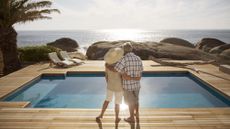 Senior couple by modern pool overlooking ocean 