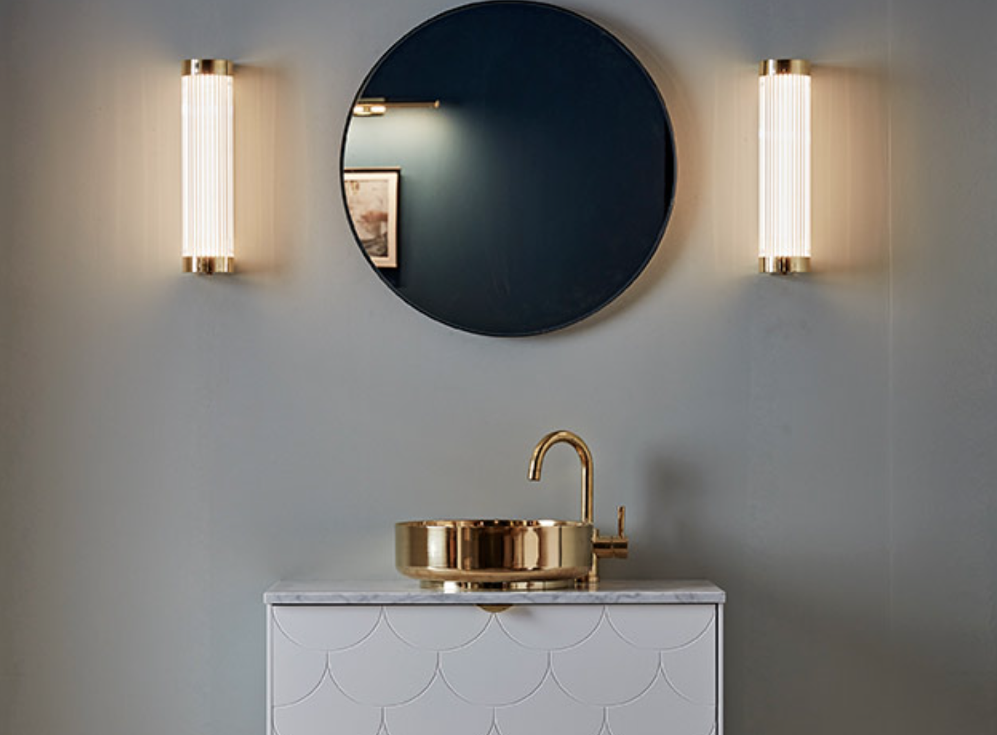 a minimalist bathroom with wall lights lit up and a brass sink