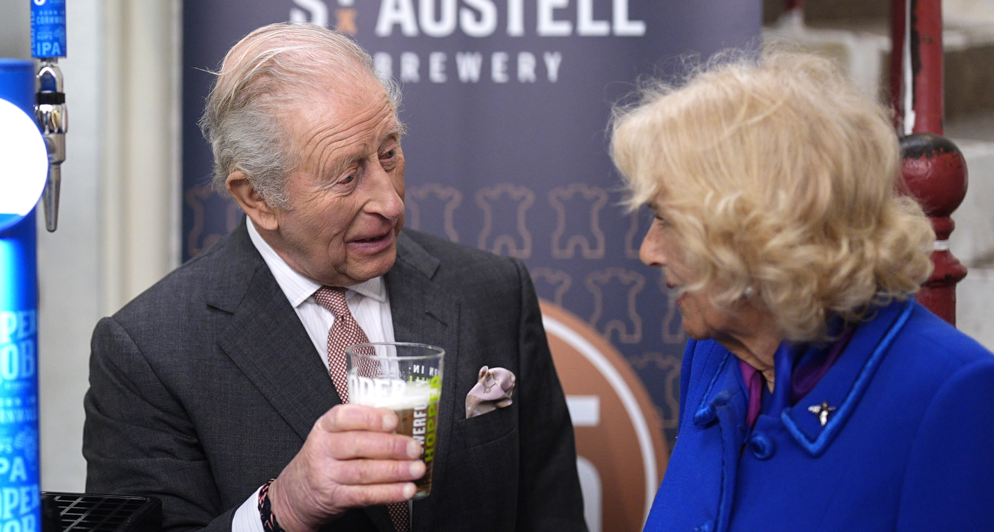 King Charles holding a beer talking to Queen Camilla 