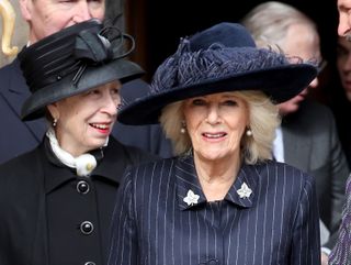 Queen Camilla and Princess Anne wearing dark coats and hats smiling