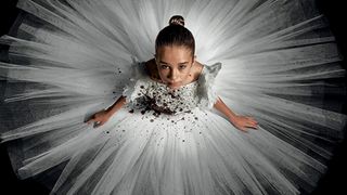 a girl in a white dress stained with blood, as a circular tutu fans around her