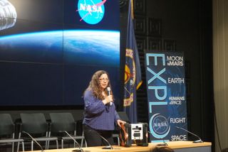 Maria G. Bualat, Astrobee project manager at NASA's Ames Research Center, speaks about the Astrobees at a news conference. In front of her sits an example of an Astrobee robot.