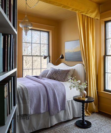 small bedroom with two large windows, a nook bed created with curtains and walls all in yellow with a wavy striped headboard, bed skirt, and small black bedside table