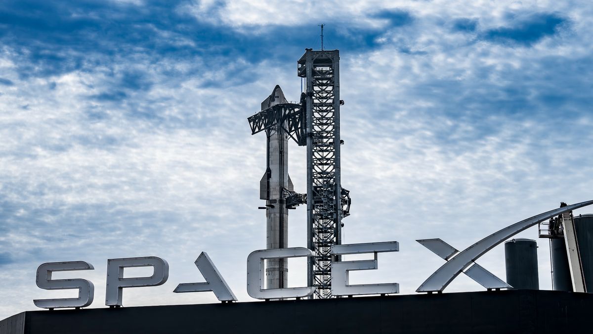 a large silver rocket stands next to its launch tower, with a large sign reading &quot;spacex&quot; in the foreground