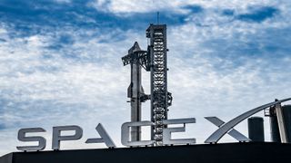 a large silver rocket stands next to its launch tower, with a large sign reading "spacex" in the foreground