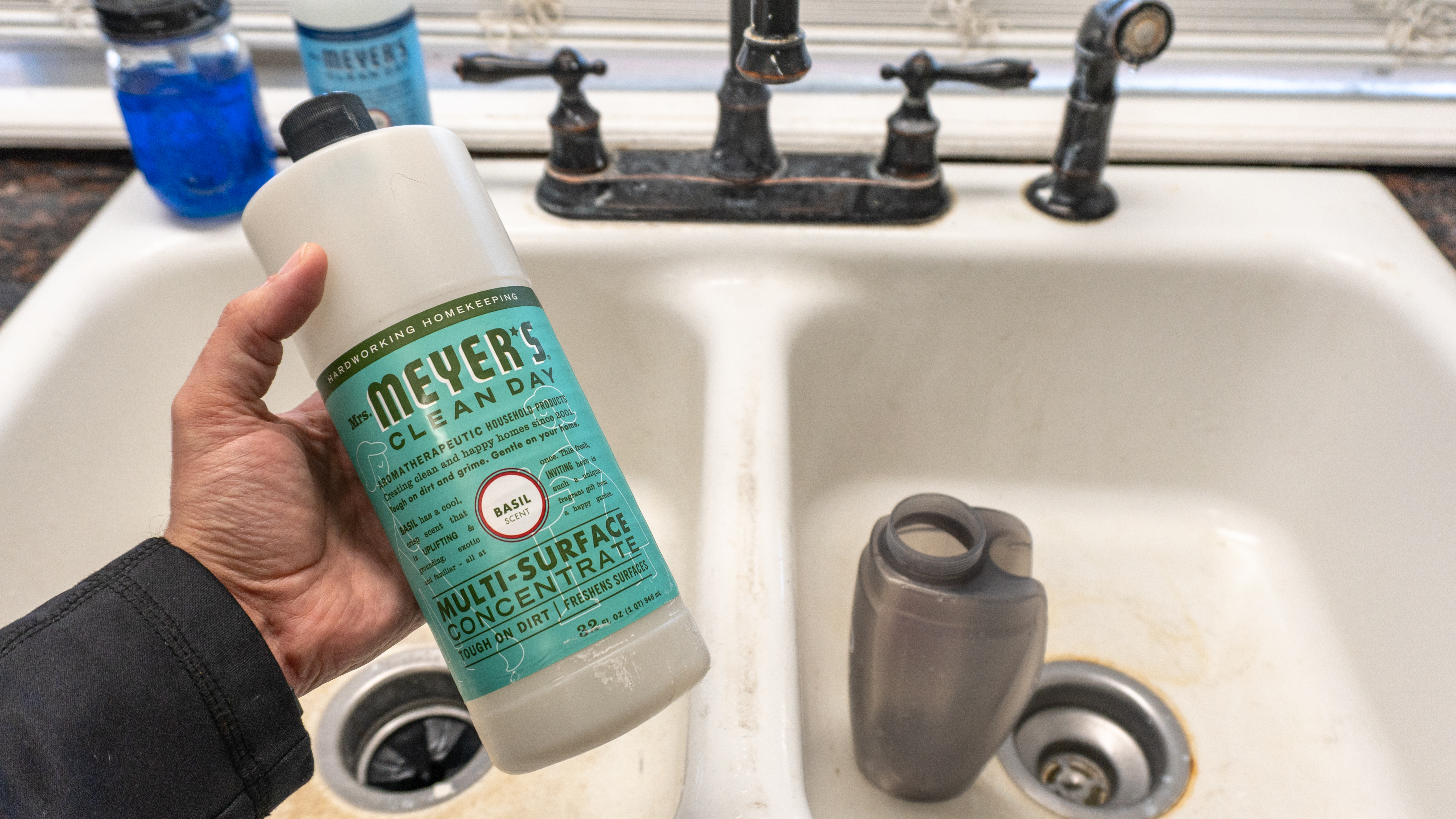 A person holding a near-empty bottle of Mrs. Meyer's Clean Day in front of a sink