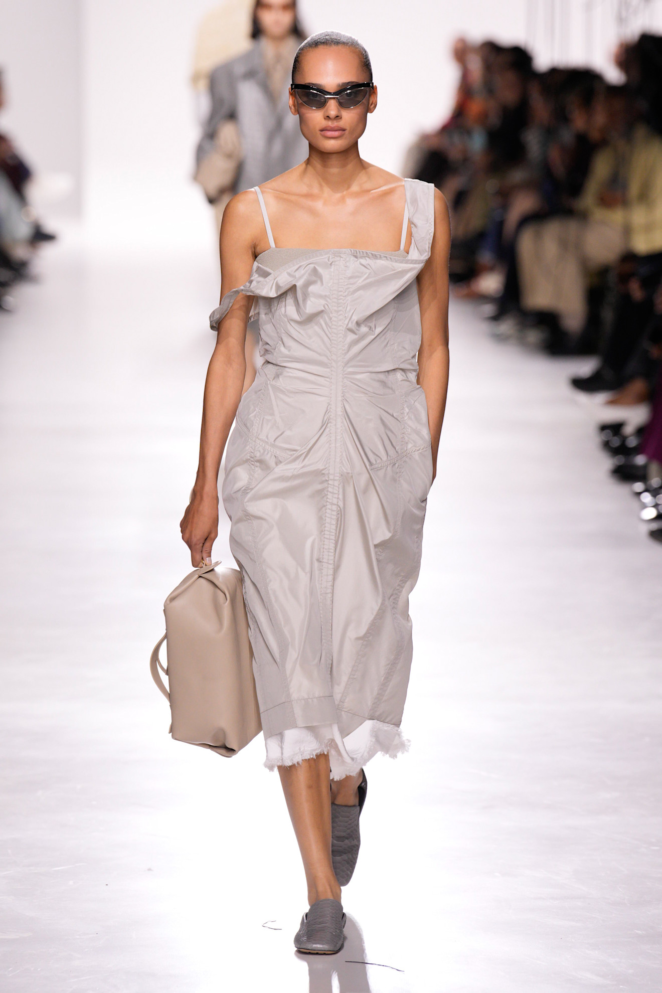 Bottega Veneta model walking in the S/S 26 show wearing a slip dress with a tan dopp kit. 