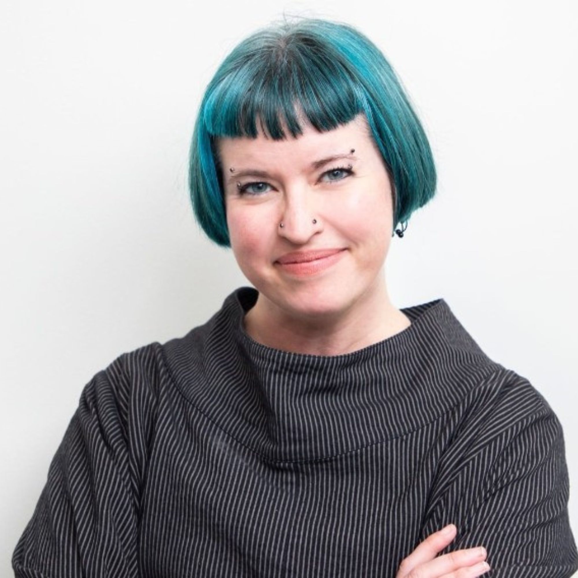 A picture of Rachel Waldron, a woman with a blue bob wearing a gray jumper against a white background