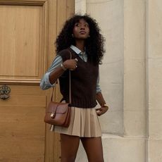 Emmanuelle Koffi captures the essence of Parisian fall in this preppy ensemble with a pleated miniskirt. She rolls up the sleeves on her striped blue button-down styled under a sweater vest. 