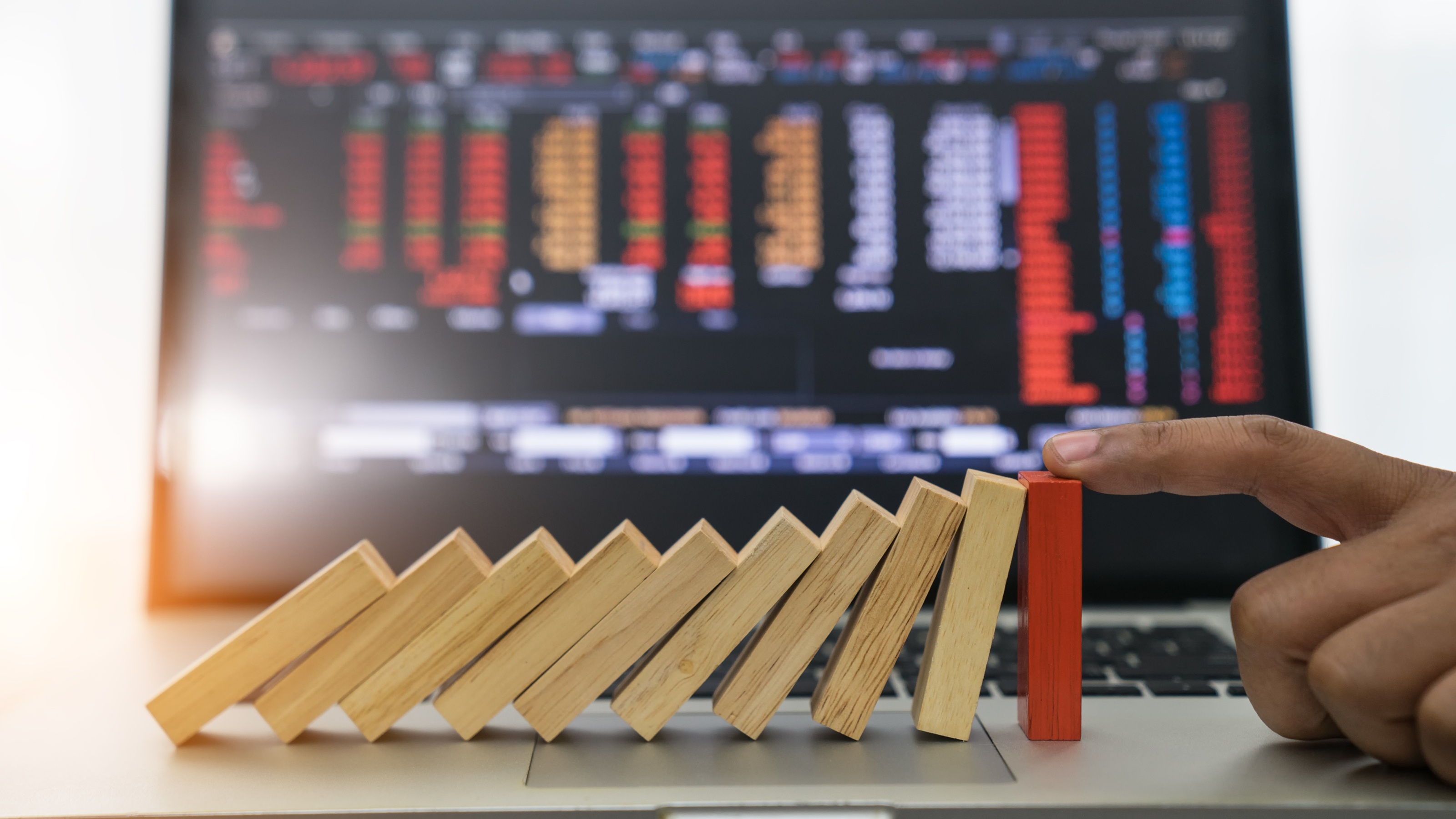 Wooden blocks fall like dominoes against a red block that stops them. A trading screen is in the background.