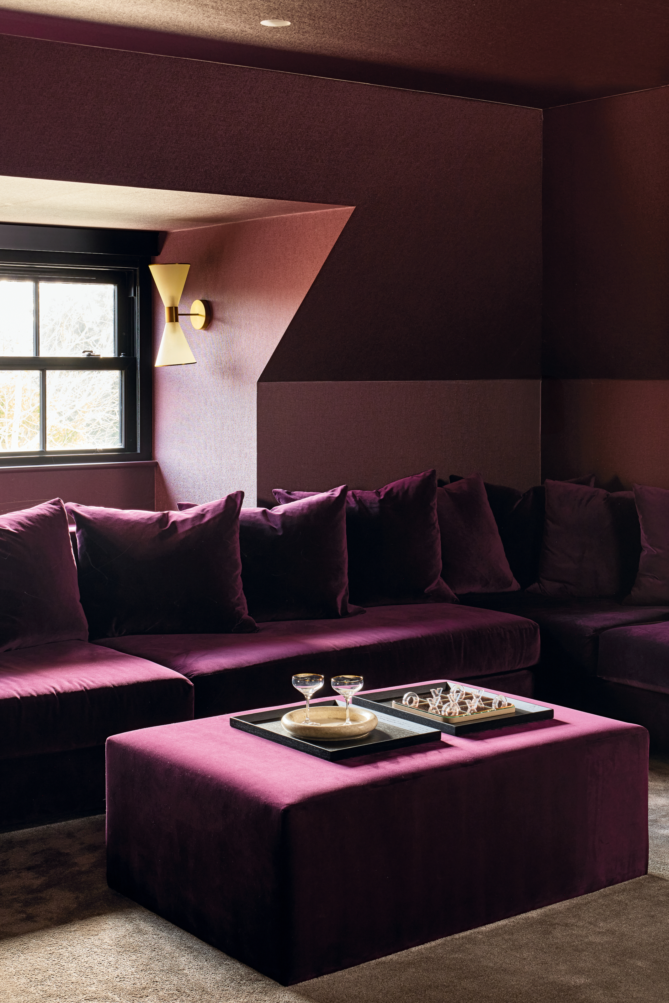 Den with plum-painted walls and ceiling, purple sofa and ottoman, and brass wall light