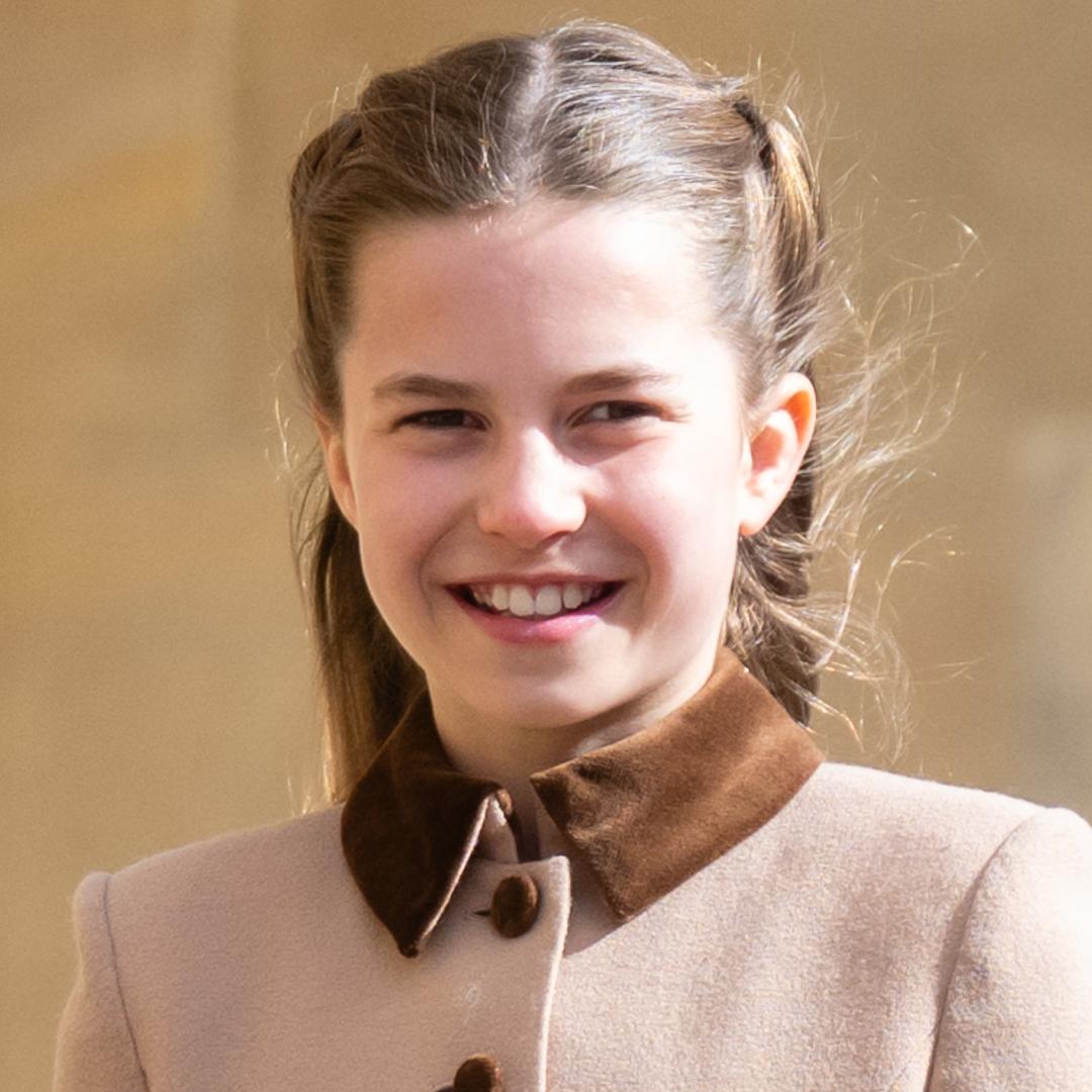 Princess Charlotte wears a light brown coat with a dark collar and smiles