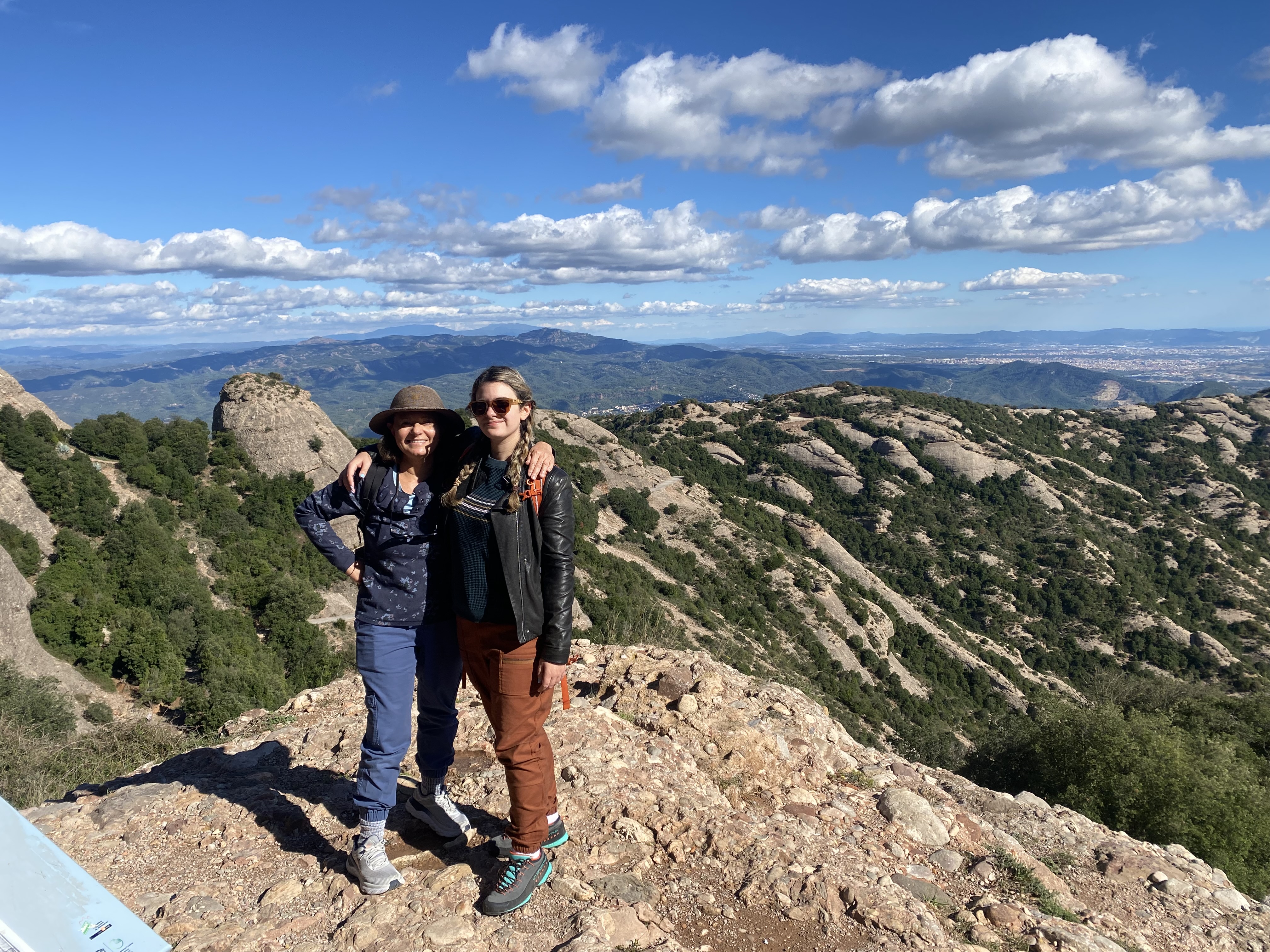 A young woman and her mother in hiking clothes stand on a rocky outcrop in Montserrat, Spain.