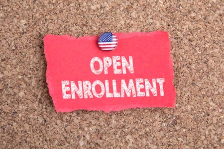 OPEN ENROLLMENT concept. Flag of the United States Of America on a pin. Red note and cork background.