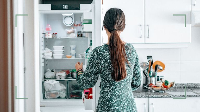 Woman in green dress standing in front of a full fridge contemplating how to clean a fridge