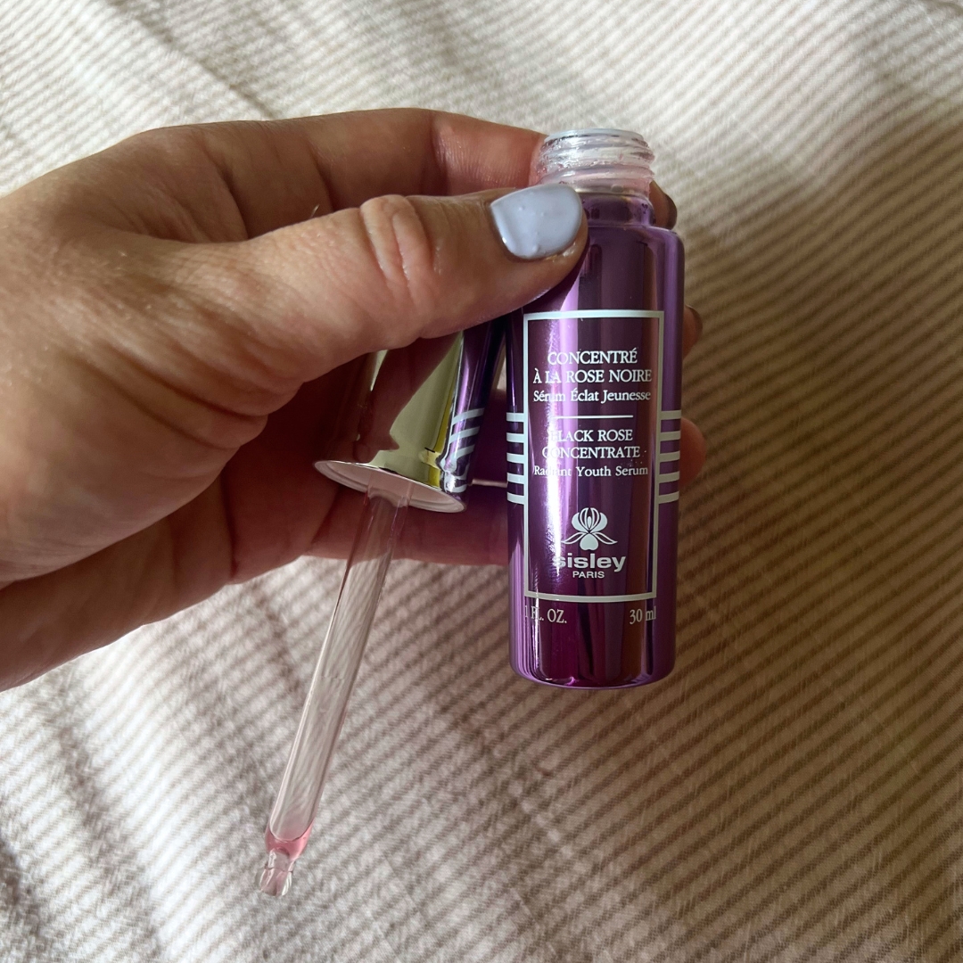 Hand holding empty purple bottle of Sisley Paris Black Rose Concentrate Serum