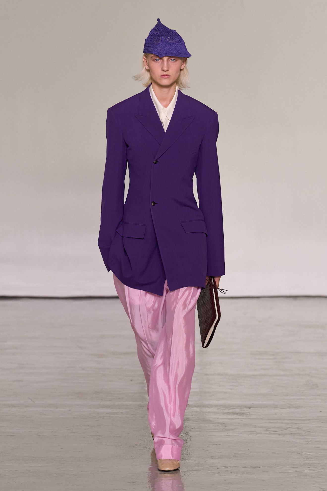 A model walking in the spring/summer 2027 Bottega Veneta show during Milan Fashion Week wearing a knit hat with a purple blazer and pink pants.