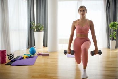 A woman performing a dumbbell lunge as part of a leg workout 