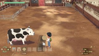 Story of Seaons: A Wonderful Life - a player holds cow fodder in their hands and waits to put it in a trough for a cow in a barn