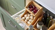 Hero shot of IKEA's stacked wooden food organizers in a deep, open kitchen drawer. It's filled with onions and garlic on top, and potatoes in its lower level.