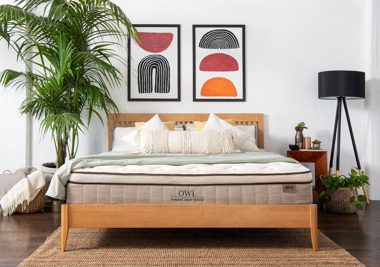 Mattress sales image of Nest Bedding Owl natural latex hybrid in bedroom on bed, with jute rug, large plant, black floor lamp and wall prints above bed