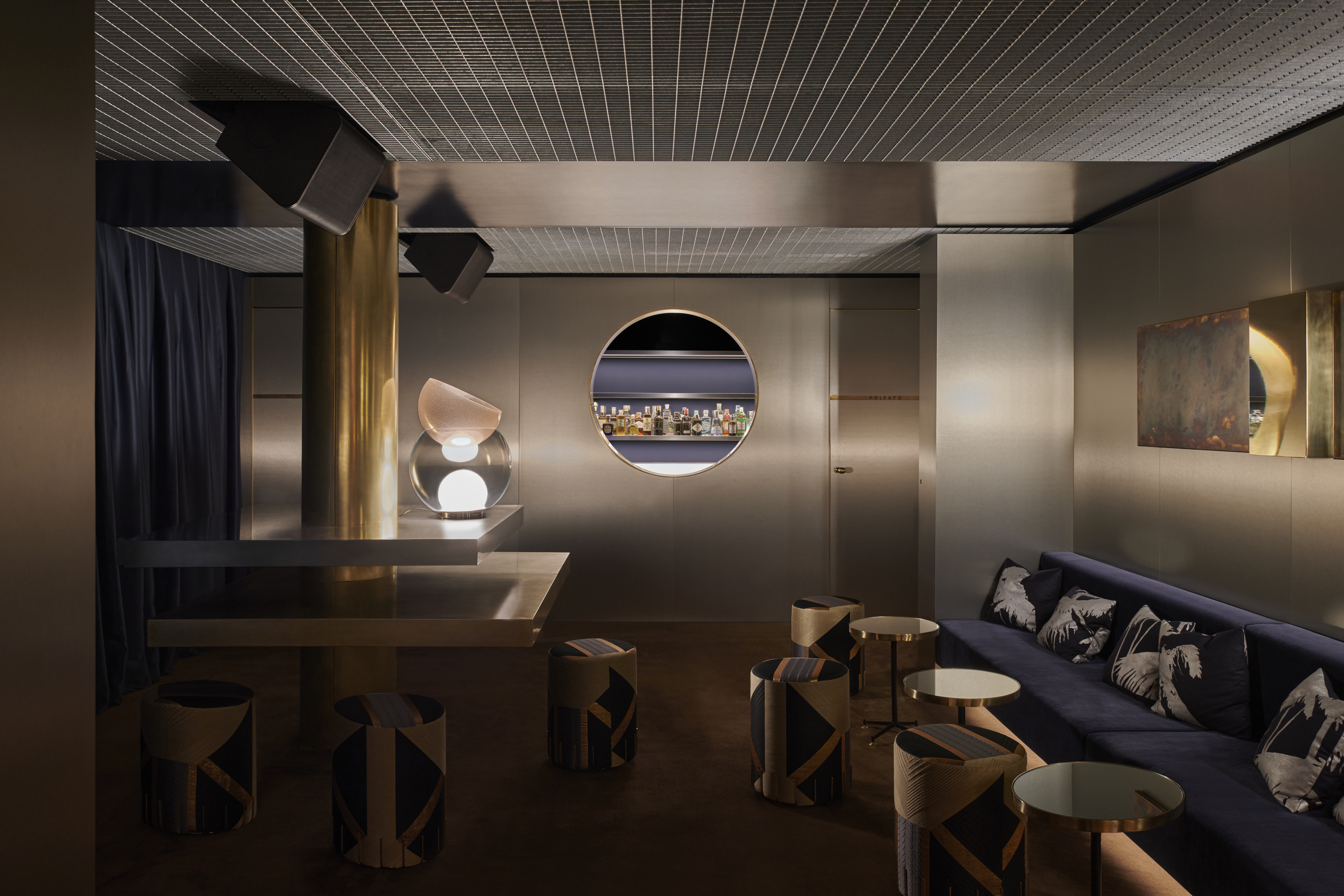 Two rooms of a restaurant, the first one dressed in brushed stainless steel, with sculptural lighting, plush velvety banquettes in sea blue, and textural delays, the other, with wall-wide neon lighting, checkered floors, and round-edged detailing.